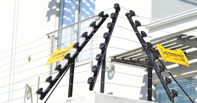 Nemtek original photograph of wall-top electric fencing with angled brackets and warning signs